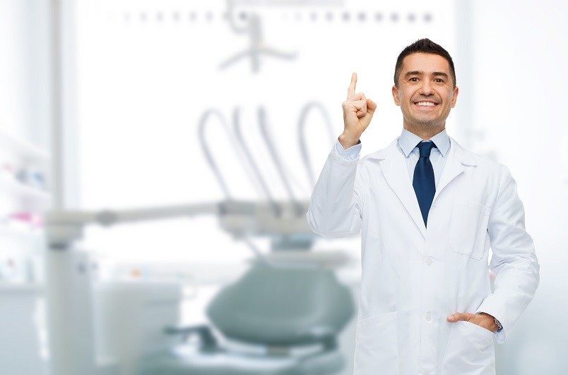 healthcare, profession, gesture, stomatology and medicine concept - smiling male middle aged dentist pointing finger up over medical office background